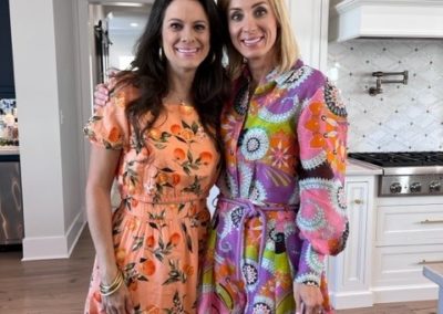 Two women in colorful dresses stand next to each, smiling for photo.