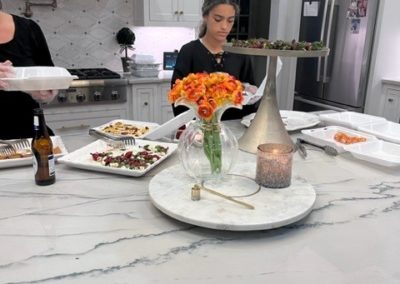 A girl preps food in a large kitchen. Flowers and takeout containers are visible on the counter in front of her.