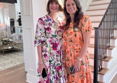 Two women in colorful dresses smile in front of a staircase.