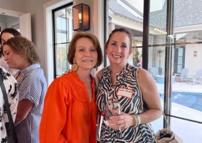 Two women, one holding a wine glass, smile and pose.